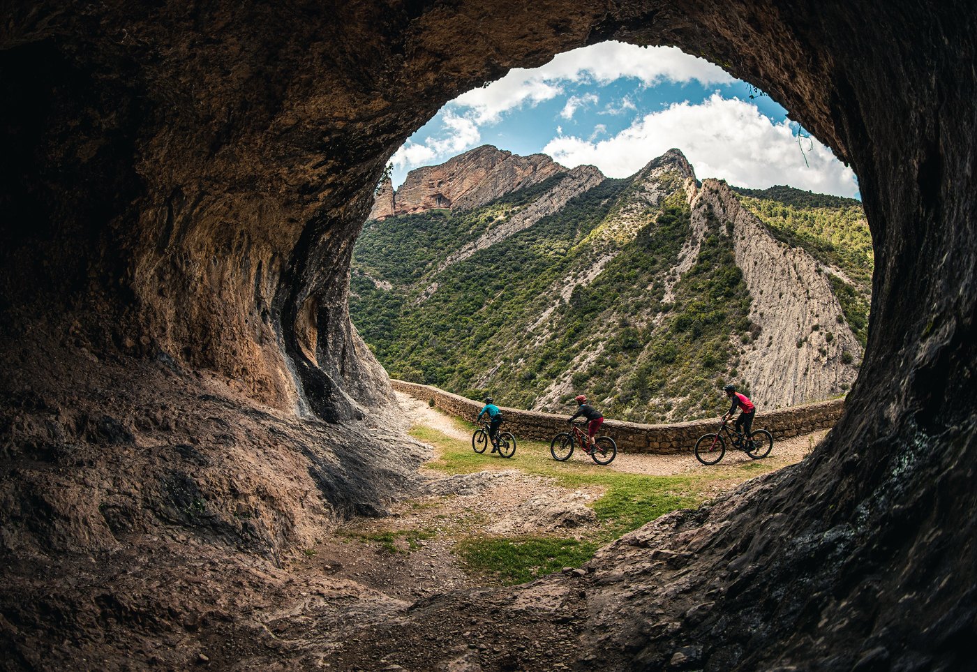 Tres ciclistas de montaña bajo un gran arco de roca