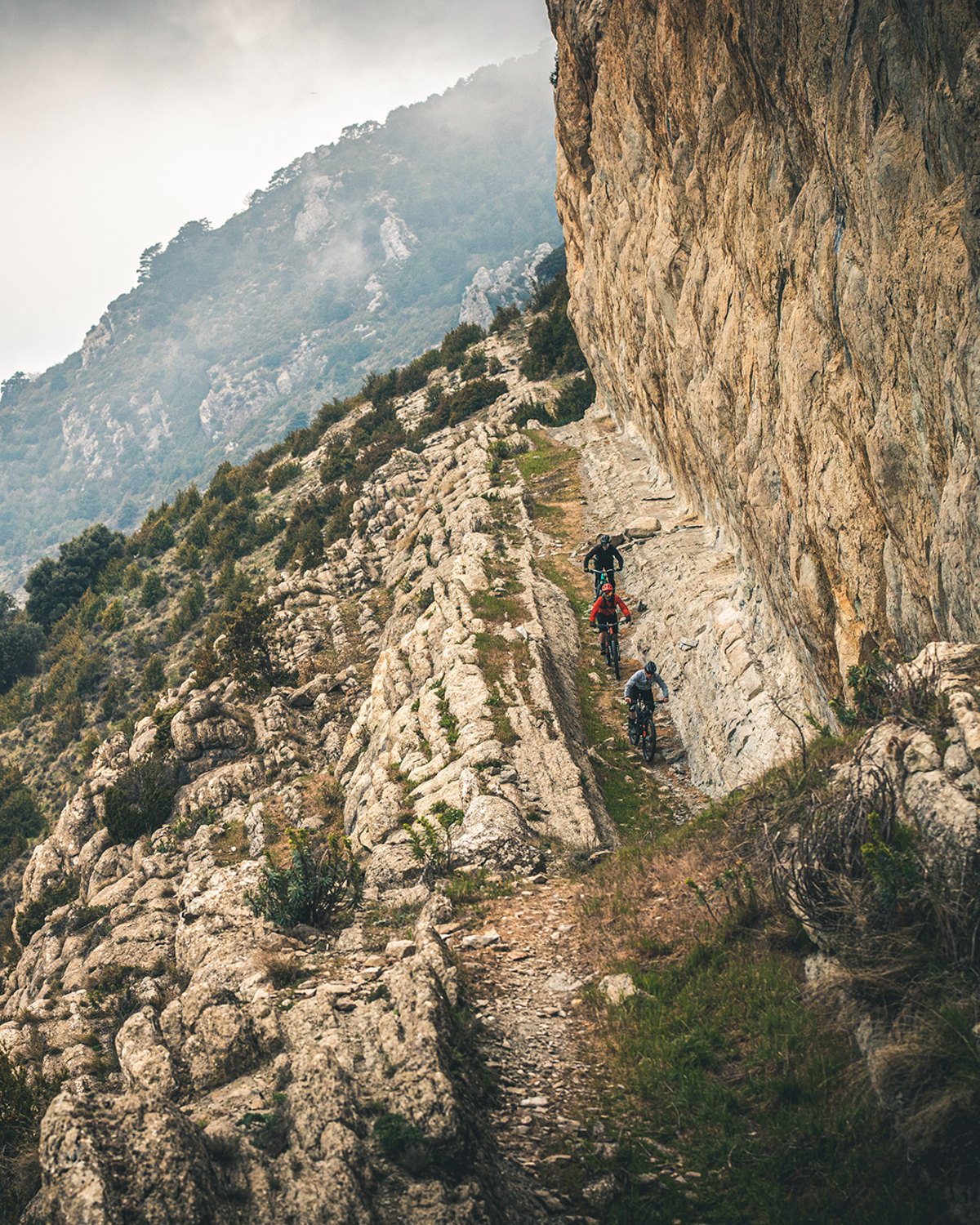 Ciclistas de montaña en un sendero al pie de una pared de roca